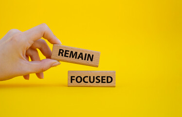 Remain focused symbol. Concept words Remain focused on wooden blocks. Beautiful yellow background. Businessman hand. Business and Remain focused concept. Copy space.