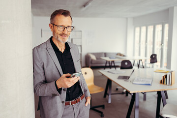 mature businessman standing with cellphone in modern office