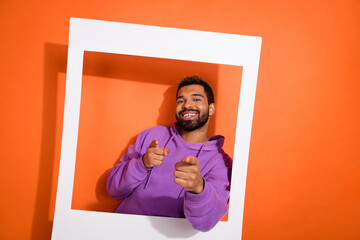 Portrait of positive friendly person point fingers camera you through paper window isolated on orange color background