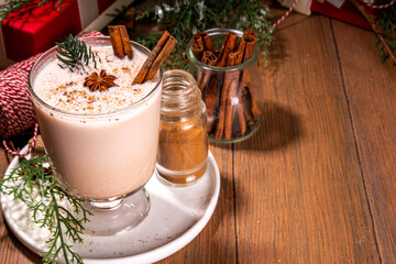 New Year Christmas creamy spicy cocktail – Eggnog, Cola de mono. Hot winter autumn drink with cream milk, eggs, rum, cinnamon and nutmeg in glass on wooden background with Christmas decoration
