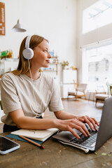 Young beautiful long-haired smiling woman in headphones typing on laptop