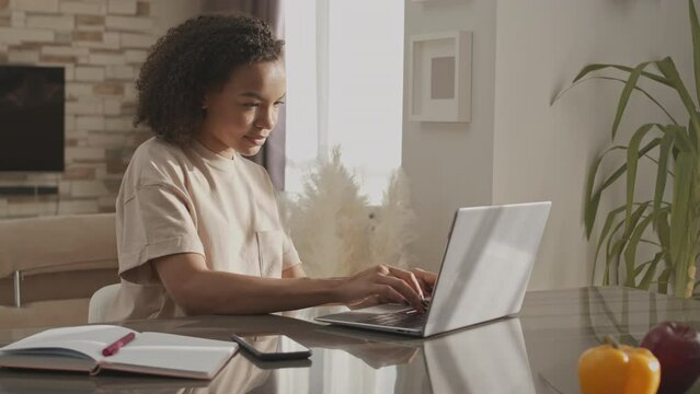 Waist up slowmo of Biracial girl in her early 20s using laptop while working or studying from home