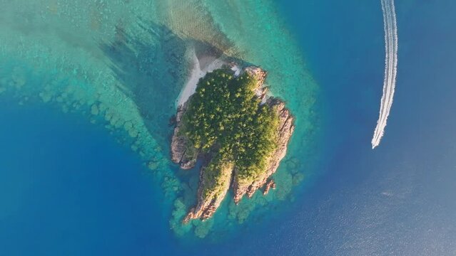 Aerial footage of a boat going around Arkhurst Island, a small islet near Hayman Island, a luxury resort hotel in the Whitsunday Islands group near the Great Barrier Reef in Queensland, Australia.