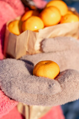 Woman in a pink coat holds a craft bag with tangerines in her hands, walking in a snowy winter park.Hands in mittens close-up.Festive mood.New Year,Christmas, winter concept.