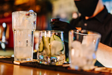 hands of a bartender with black gloves making cocktail on a bar counter.