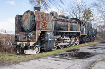 An old and dilapidated historic PKP steam locomotive standing on a siding on a gloomy autumn day. Rail.