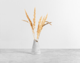 Fluffy bouquet of ears of wheat and dried flowers in a plaster vase on a gray concrete table, front view, copy space. Home decor.