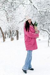 Fototapeta na wymiar A beautiful dark-haired young woman in a pink faux fur coat with fir branches in her hands in a winter park.New Year,Christmas and eco-friendly concept.Selective focus.
