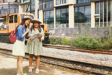 Fototapeta premium Sexy girl, fragile figure with a close friend, fat plus size, cute, high season traveling together happily. Look at the route from the map waiting for the train at the suburban station landmark.