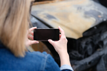 Insurance agent woman photographs burned-out car on smartphone
