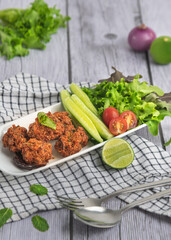 Fried Pork Larb (lab tod) in long plates with vegetable side dishes  on wood background top view.
