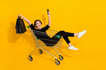 Photo of cute excited lady wear black shirt rising arms riding shopping tray rising device bags...