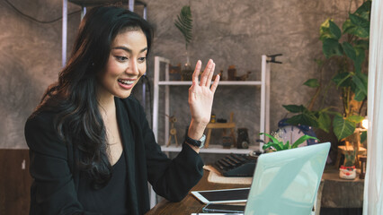 Young Asian professional businesswoman discussing business with her business partner via video conferencing using a laptop in a modern office space.