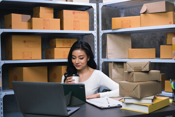 Fototapeta na wymiar young Asian businesswoman owner runs e-commerce, prepares parcels and checks orders to deliver to customers on his laptop at home. Sell products online through the Internet, online business concept