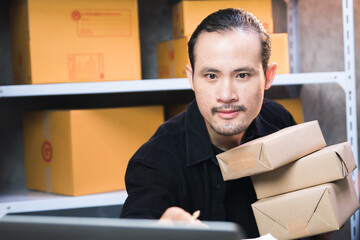 online business concept, young Asian businessman owner runs e-commerce, prepares parcels and checks orders to deliver to customers on his laptop at home. Sell products online on cyberspace