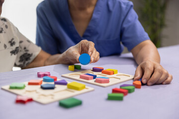 Caregiver and senior woman playing wooden shape puzzles game for dementia prevention - obrazy, fototapety, plakaty