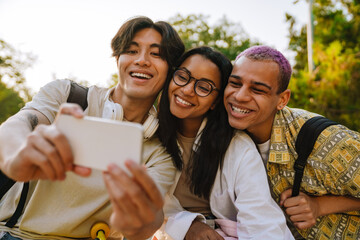 Fototapeta premium Three multiracial friends taking selfie photo in skate park