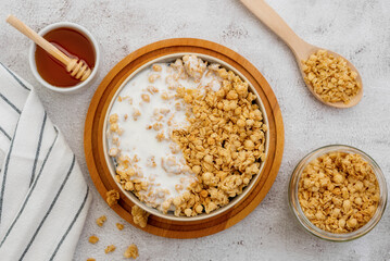 Flat lay (top view) of Crunchy oat granola cereal with fresh milk in bowl and wooden spoon isolated on background.