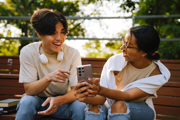 Two multiracial friends using mobile phone together in skate park