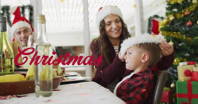 Animation of christmas over happy caucasian mother putting on santa hat on son head