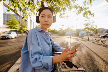 Fototapeta premium Asian woman using cellphone while picking up scooter on city street