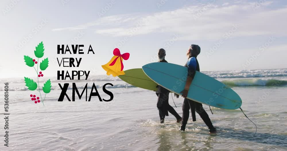 Wall mural Animation of have a very happy xmas over senior biracial couple with surfboards on beach