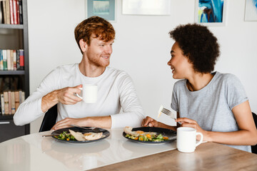 Young multinational couple smiling while having breakfast at home