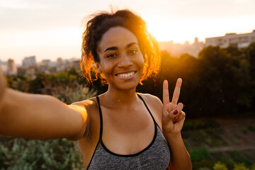 Young black woman gesturing while taking selfie photo in summer park
