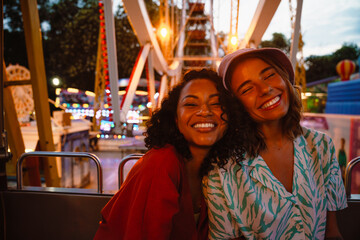 Fototapeta na wymiar Young multiracial women riding on ferris wheel in attraction park