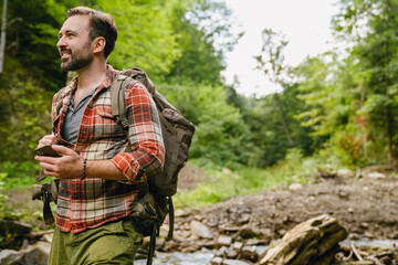 Young white man with backpack using cellphone while hiking in forest