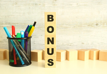 Stacked vertically wooden cubes with letters in the word BONUS on a white work table on a textured gray background.