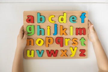 Childish hands holding alphabet wooden board with colored font letters in cells closeup isolated