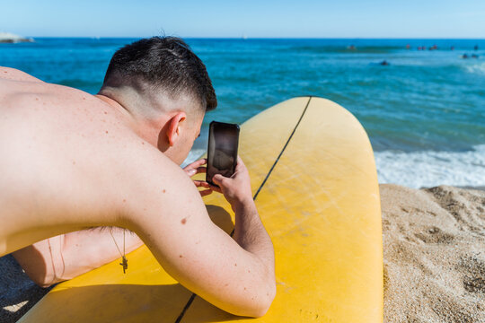 Surfer taking photo on smartphone on beach