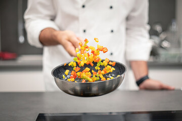 Professional chef cooking and tossing pepper mix with herbs in p