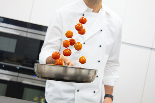 Professional chef with pan of cherry tomatoes with herbs cooking