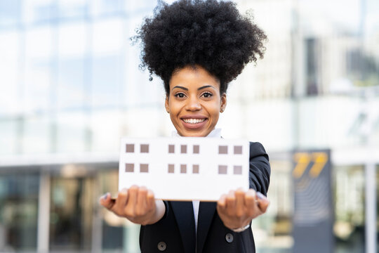 Black female architect with model of house looking at camera