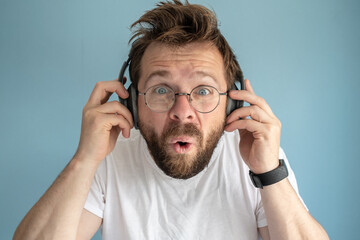 Shaggy, bearded man in headphones listens to music, he is annoyed and surprised, he does not like...