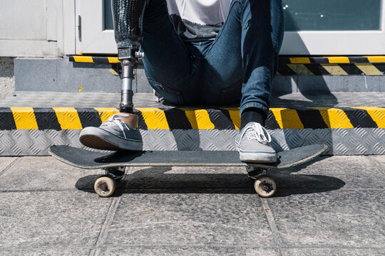 Crop skater with leg prosthesis sitting on stairs