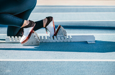 Crop athlete in crouch start position on starting blocks