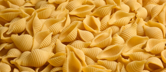 Conchiglie, Shells or Seashells Pasta Wallpaper. Spiral Raw Macaroni from Wheat flour. Close Up Top View. Uncooked Pasta Spinning. Full Frame. Food Background. Conchigliette banner with copy space