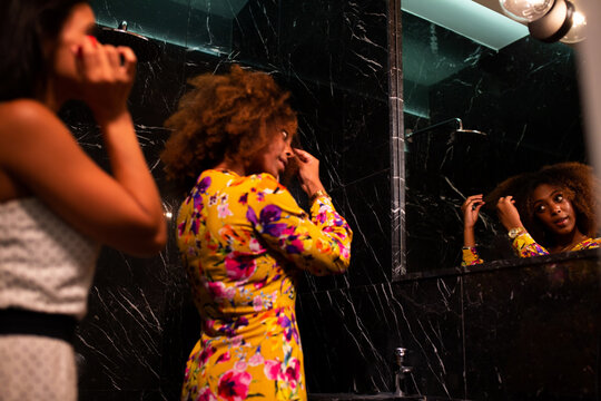 Cheerful young diverse female friends refresh makeup in bathroom