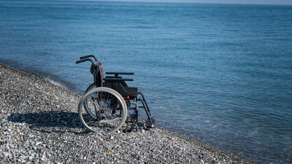 Obraz premium An empty wheelchair on a rocky seashore.