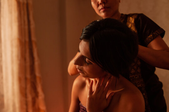 Thai female massagist giving a massage to a young woman