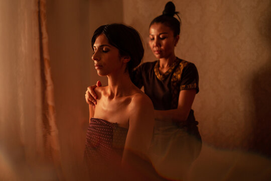 Thai female massagist giving a massage to a young woman
