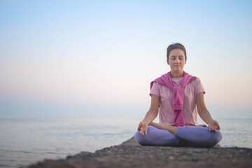 Naklejka na ściany i meble Yoga woman meditation in lotus position at pebble sea beach sunset sky horizon healthy lifestyle