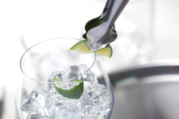 Ice tweezers rubbing a slice of lime in a glass