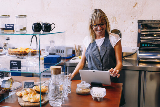 Cheerful woman standing in kitchen and watching tablet ob table
