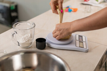 Fototapeta na wymiar Woman's hands weighing portions of dough, to make pan de muerto at her kitchen counter