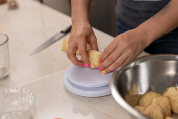 Woman's hands weighing portions of dough, to make pan de muerto at her kitchen counter