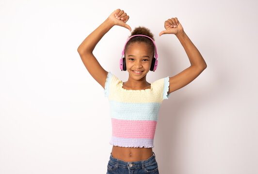 Cheerful young african american woman girl posing isolated on white background studio portrait. People lifestyle concept. Listen music with headphones, dancing